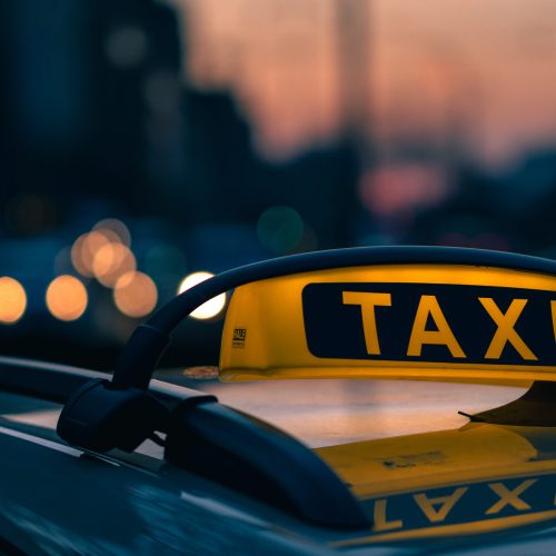 A close-up shot of a taxi sign in the warm colours of sunset with bokeh lights in the background. Urban transportation.
